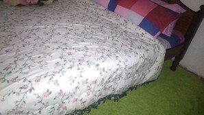 A bed with floral bedding and a wooden headboard, a green rug, and a single decorative pillow. - VIV HAVEN (Nairobi)