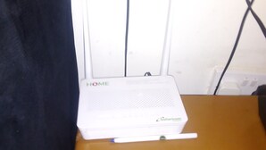 A white router labeled "HOME" and "Solarcom" on a brown surface, with visible cables and a black curtain partially obscuring the view. - VIV HAVEN (Nairobi)