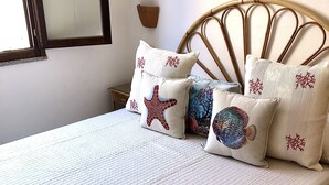 Una cama con colcha blanca acolchada y almohadones decorativos con motivos marinos.