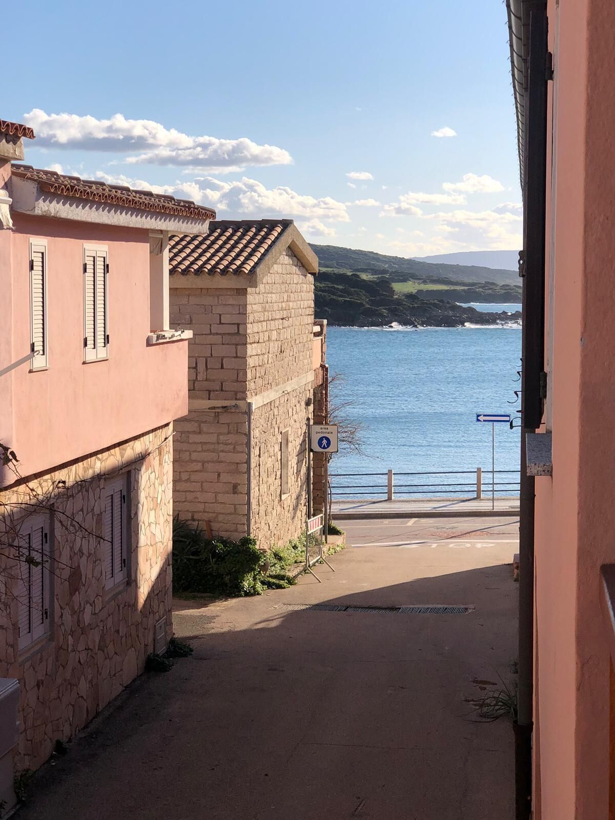 Calle estrecha que lleva a una masa de agua, con una señal para peatones, un edificio de piedra y un edificio rosa.