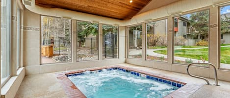 A hot tub with a wooden ceiling and large windows overlooking a backyard.