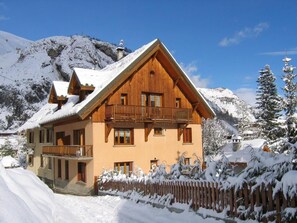 Un chalet in legno con un balcone, circondato da montagne innevate.