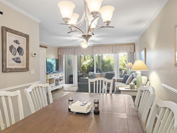 A dining area with a wooden table, white chairs, a chandelier, and a view of the outdoors.