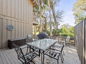 A covered outdoor patio with a dining table and chairs, a grill, and a wooden deck.