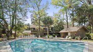 A swimming pool surrounded by lounge chairs and trees, with a building in the background. - 28 Water Oak Villa | Special Fall Rates 2026 | Golf Views | Permit #077642 (Hilton Head Island)