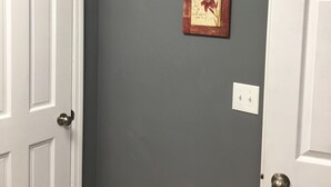 Un couloir avec un mur gris, deux tableaux encadrés, une porte blanche et un panier blanc.