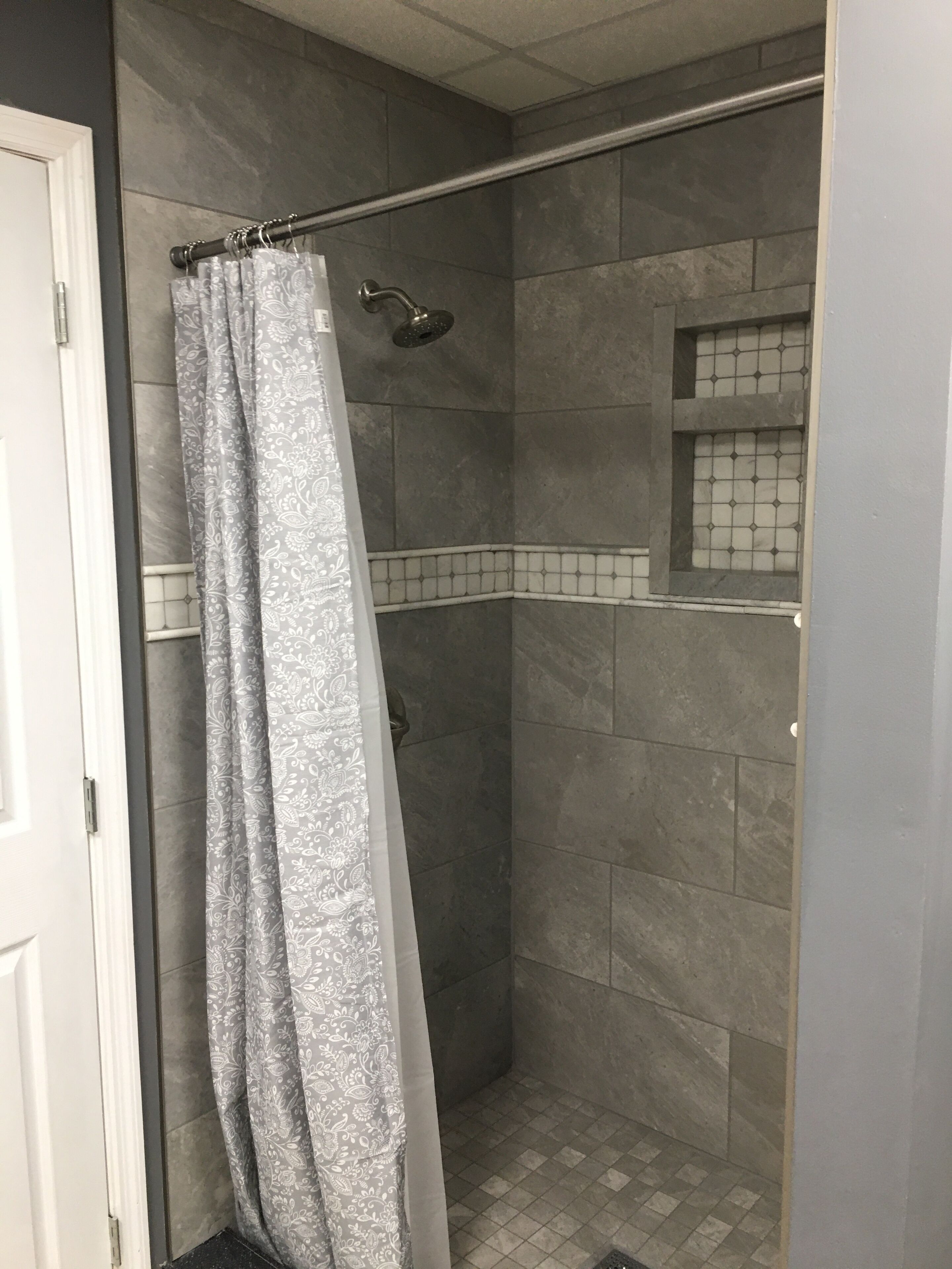 Un espace douche avec des carreaux gris, un rideau de douche et une petite fenêtre.