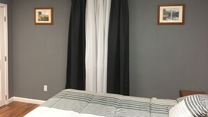 Une chambre à coucher avec un lit, deux tableaux encadrés, une fenêtre avec des rideaux noirs et blancs et un ventilateur de plafond.