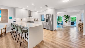 Een moderne keuken met een groot eiland, roestvrijstalen apparatuur en uitzicht op een eetgedeelte.
