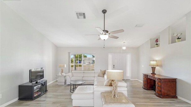 A spacious living room with a white sofa, a coffee table, a TV stand, and a wooden desk. - Calling all boaters and fishermen!  Canal front home with 10k lb boat lift! (North Fort Myers)