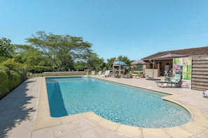 A swimming pool with lounge chairs and a covered area.