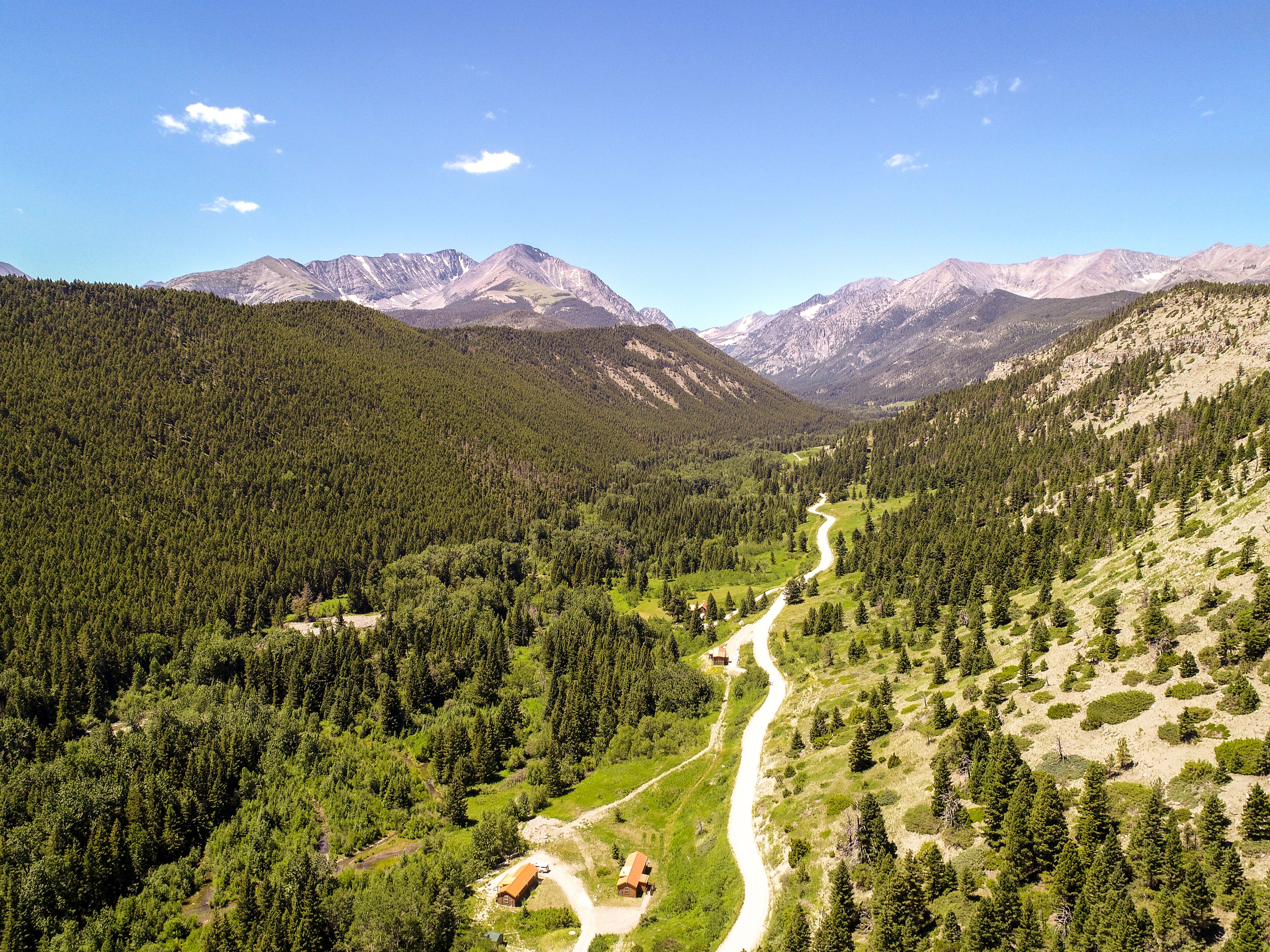 A mountainous landscape with a winding road, dense forests, and a clear sky.
