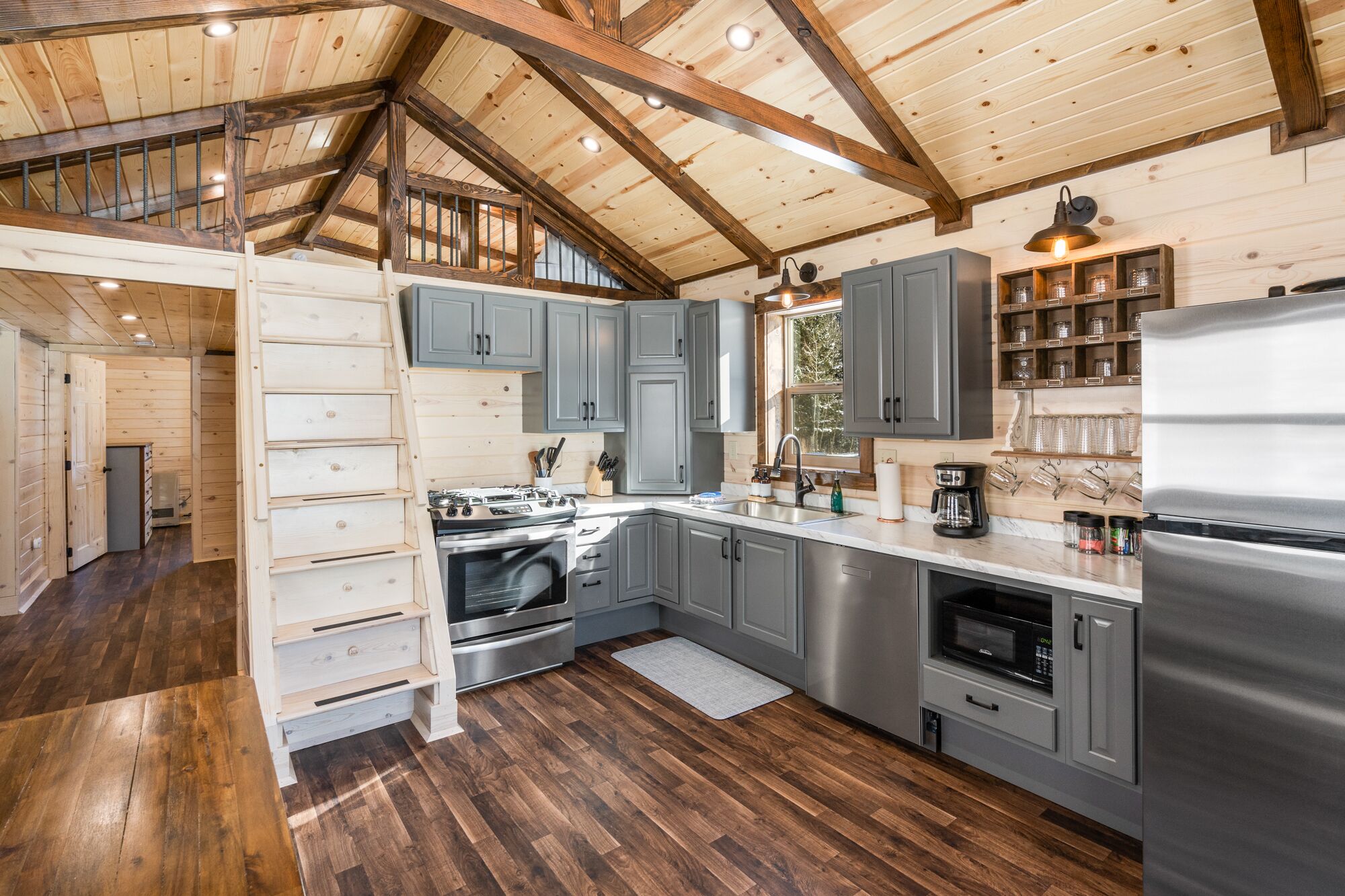 A modern kitchen with wooden beams, grey cabinets, stainless steel appliances, and a wooden floor.