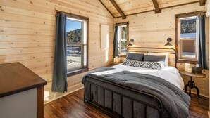 Un dormitorio de cabaña de madera con una cama, lámparas de noche y vista a un paisaje nevado.