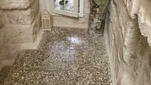 A narrow stone-walled room with a small window, a tiled floor, and a vase with sunflowers.