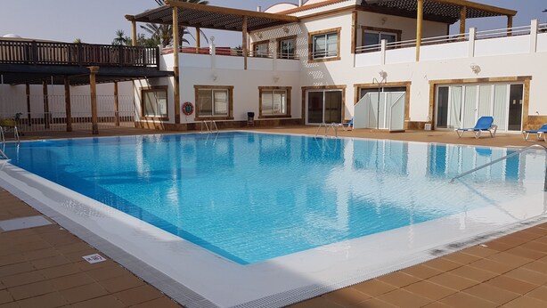 En swimmingpool med krystalklart, blåt vand, omgivet af en fliseterrasse. Liggestole og en redningsplatform er i nærheden.