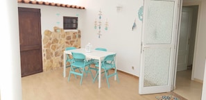 A dining area with a white table and turquoise chairs, a stone wall, a wooden door, and a frosted glass door.