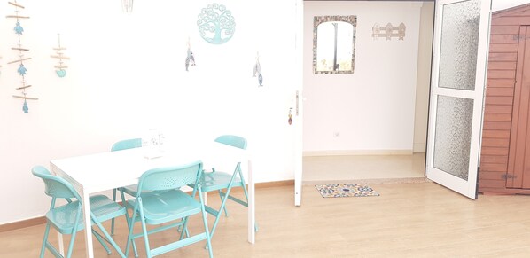 A room with a white table and teal chairs, a patterned rug, and wall decorations including a tree and fish.