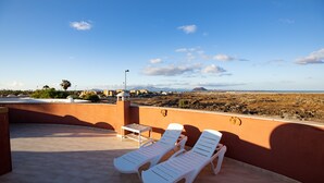 En tagterrasse med to hvide liggestole, et lille bord og udsigt over et ørkenlandskab.