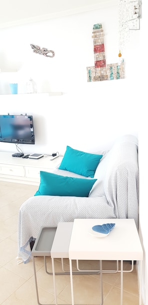 A modern living room with a sofa, a small table, a TV, and a decorative wall piece.