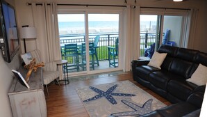 A living room with a black leather sofa, a starfish-patterned rug, and a view of the ocean through large sliding doors. - Beachside Sandcastle - Oceanfront, 1st-level Condo in Ponce Inlet (Ponce Inlet)