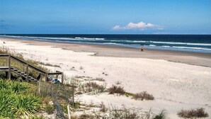 A beach with a wooden staircase leading down to the sand, a clear sky, and the ocean in the background. - Beachside Sandcastle - Oceanfront, 1st-level Condo in Ponce Inlet (Ponce Inlet)