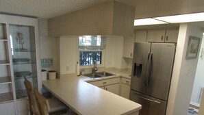 A compact kitchen with a stainless steel refrigerator, a sink, and a window. - Beachside Sandcastle - Oceanfront, 1st-level Condo in Ponce Inlet (Ponce Inlet)