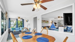 A spacious living area with a wooden dining table, blue cushions, and ceiling fans. - Mermaid Tale 2 Bedroom Condo by RedAwning (Bradenton Beach)