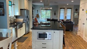 Una cocina moderna con armarios blancos, una isla central con microondas y un comedor con mesa y sillas blancas.