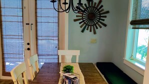 Un comedor con una larga mesa de madera, sillas blancas, una araña y un adorno en la pared.
