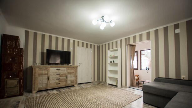 A living room with a flat-screen TV, a wooden cabinet, a patterned rug, and a gray sofa. - Stunning 5 Bed House in Campulung Moldovenesc (Campulung Moldovenesc)