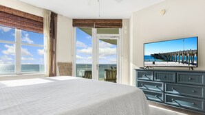 A bedroom with a large bed, a television displaying a beach scene, and a view of the ocean through a sliding door.