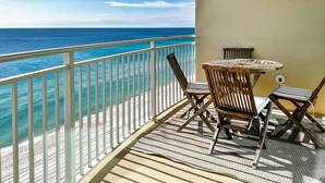 A balcony with a view of the ocean, a round table, two chairs, and a small stool.