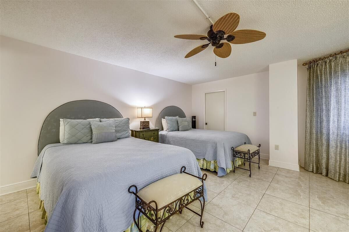 Une chambre avec deux lits, un ventilateur de plafond, des lampes de chevet, une porte et une fenêtre avec des rideaux.