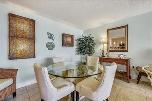 A dining area with a glass table surrounded by four chairs, a potted plant, and decorative wall art.