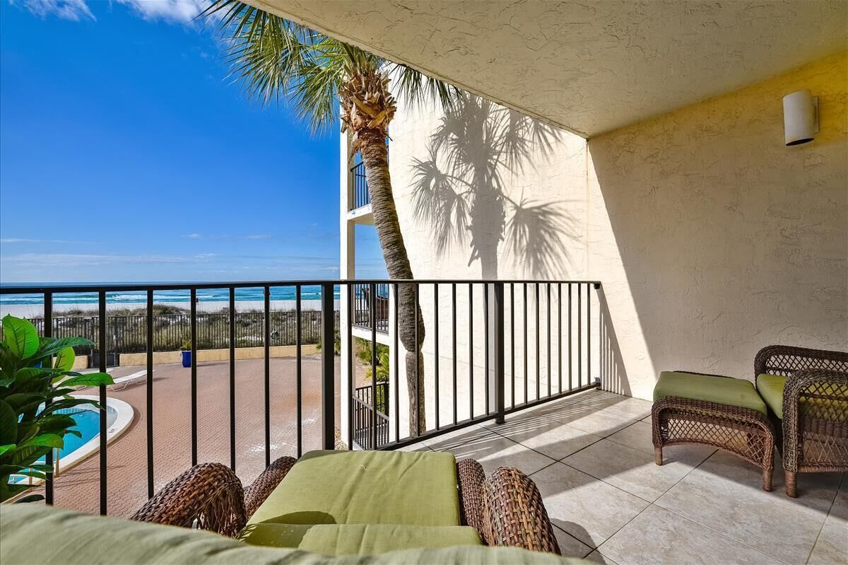 A balcony with wicker furniture, a pool, and a view of the ocean.