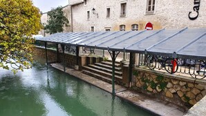 A covered outdoor area with steps leading down to a canal, a stone wall, and a building with a sign that reads "Cam."