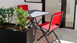 A patio with a table and two red chairs, a potted plant, and a sliding glass door.