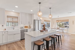 A modern kitchen with white cabinetry, a large island with stools, stainless steel appliances, and pendant lighting.