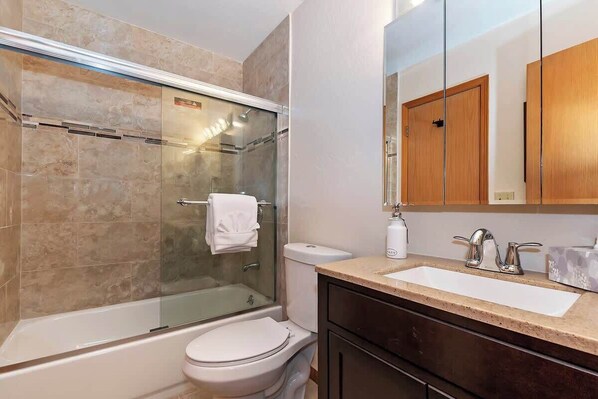 A bathroom with a glass-enclosed shower, a toilet, a sink with a marble countertop, and wooden cabinets. - The Outer Rim | Fireplace · Near Slopes (Big Bear Lake)