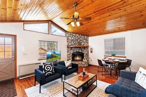 A cozy living room with a stone fireplace, wooden ceiling, and a large TV. - The Outer Rim | Fireplace · Near Slopes (Big Bear Lake)