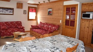 A cozy room with a wooden bed, a red sofa, a wooden table, and a wooden cabinet with a microwave.