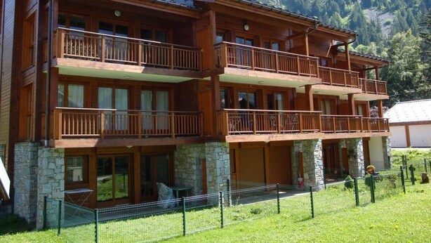 A multi-story wooden building with balconies, stone foundation, and a mountainous backdrop.