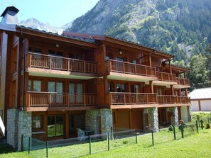 A multi-story wooden building with balconies, stone foundation, and a mountainous backdrop.