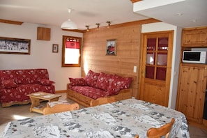 A cozy room with a bed, a red sofa, a wooden cabinet, and a television.
