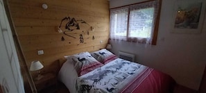 A bedroom with a wooden headboard, a bed with patterned bedding, a nightstand with a lamp, and a window with a view.
