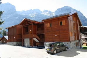 A wooden chalet with a stone foundation, a balcony, and a car parked in front.