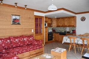 A cozy living room with a red sofa, wooden walls, and a dining area with a table and chairs.