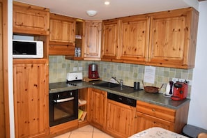 A compact kitchen with wooden cabinets, a microwave, a toaster, a coffee maker, and a dishwasher.