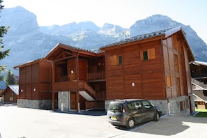 Een houten lodge met een stenen fundering, meerdere balkons en een auto ervoor geparkeerd.